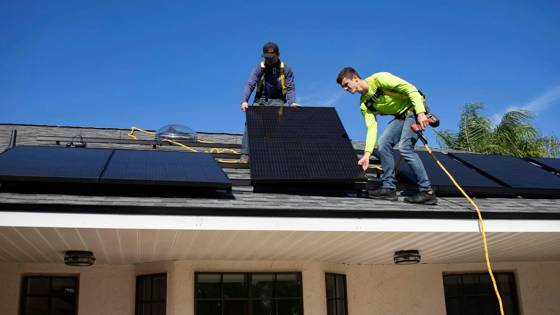 Two Prime Volt installers fitting panels on a residential roof under a clear sky